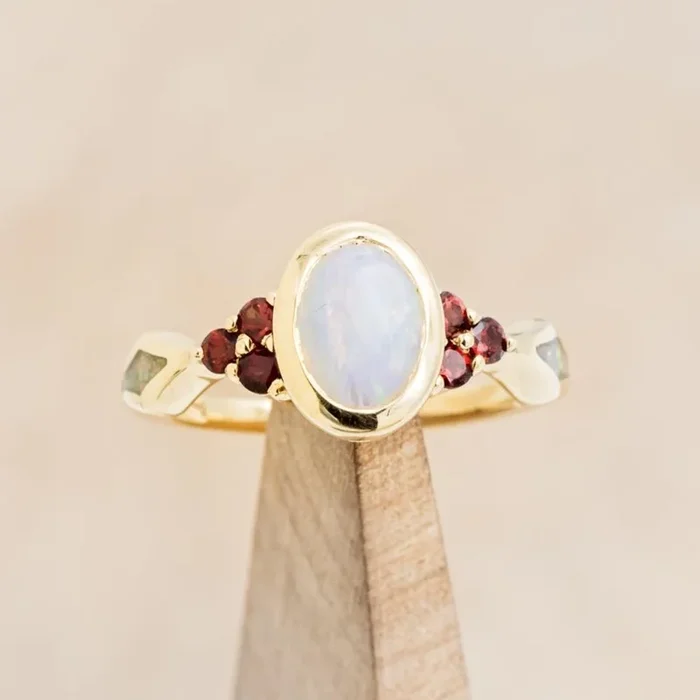 “AGATHA” – BEZEL SET OVAL CABOCHON CUT WHITE OPAL ENGAGEMENT RING WITH GARNET ACCENTS AND FIRE & ICE OPAL INLAYS