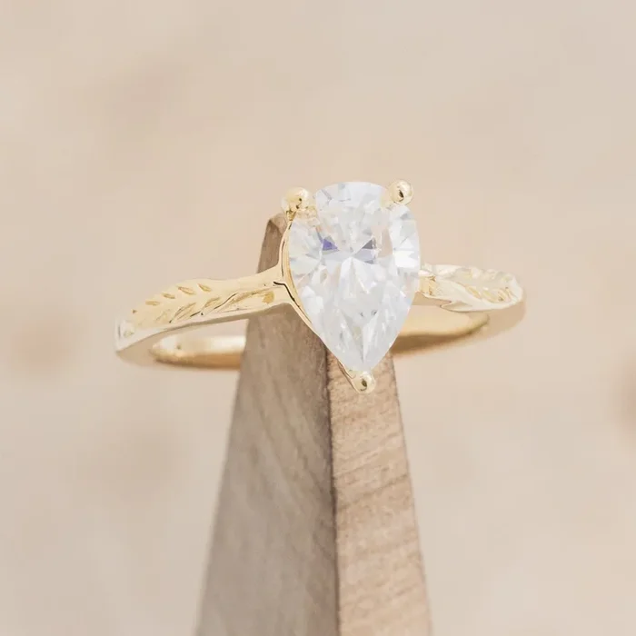 “HOPE” – PEAR CUT MOISSANITE SOLITAIRE ENGAGEMENT RING WITH FEATHER ACCENTS